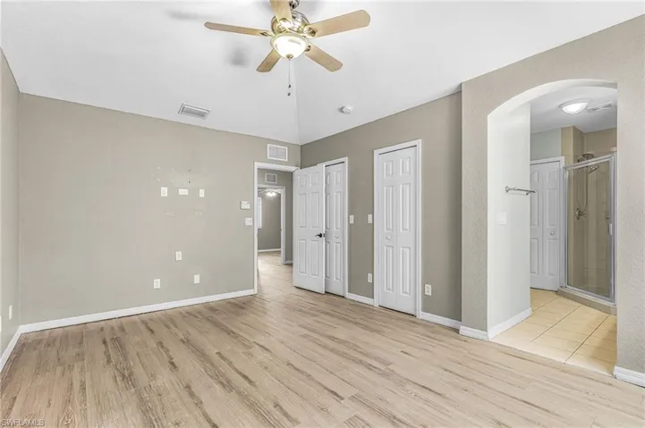 Unfurnished bedroom with multiple closets, light wood-type flooring, arched walkways, ensuite bath, and ceiling fan