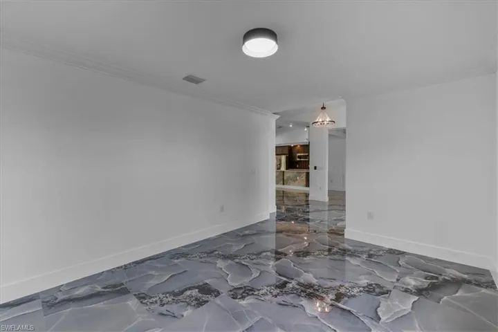 Empty room with dark marble finish floors, crown molding, and a chandelier