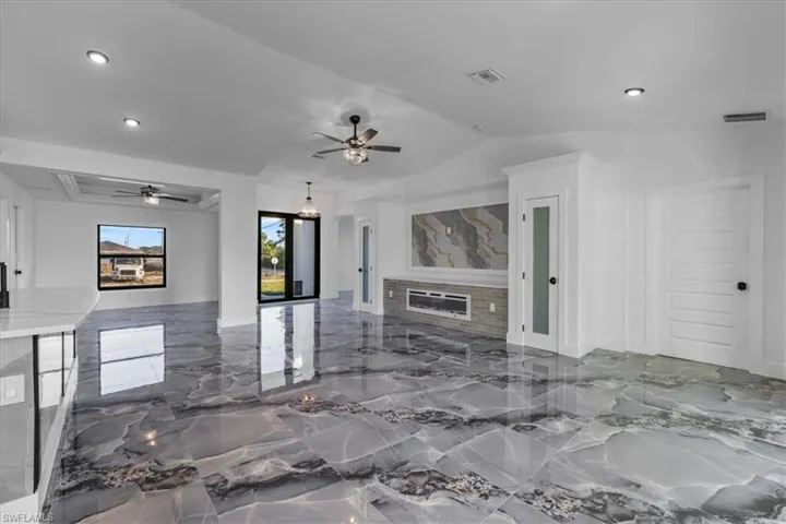 Living area featuring marble tiled floors, a glass covered fireplace, recessed lighting, a ceiling fan, and lofted ceiling