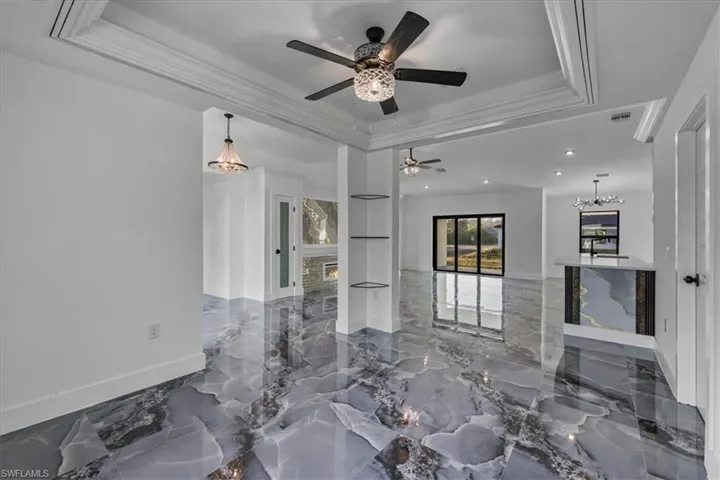 Living room featuring a chandelier, dark marble finish flooring, a glass covered fireplace, a tray ceiling, and crown molding