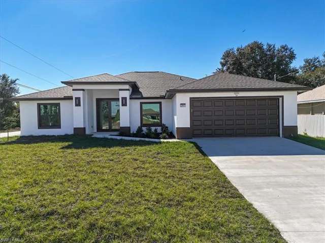Prairie-style home with stucco siding, a front yard, driveway, and a shingled roof