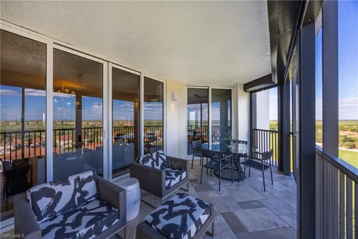 Sunroom / solarium with a textured ceiling, expansive windows, a patio, outdoor dining area, and stone tile floors