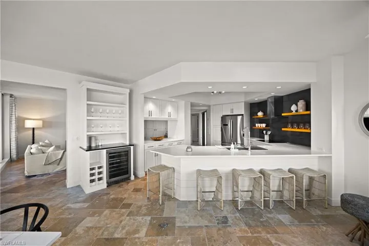 Kitchen featuring white cabinetry, open shelves, a breakfast bar, stone tile flooring, and wine cooler