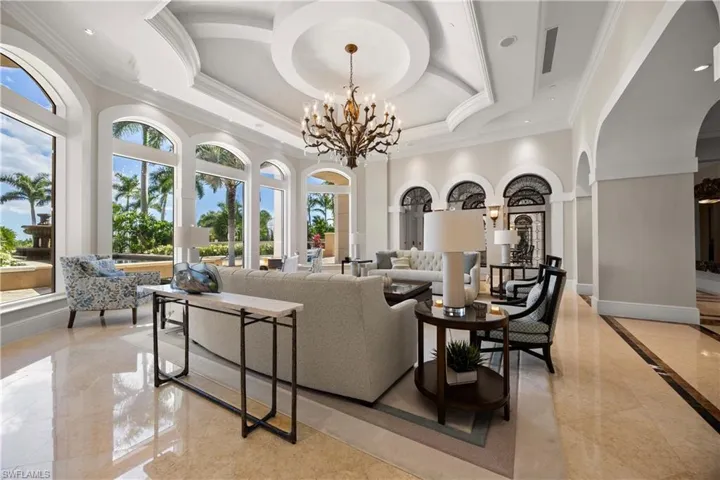 Living area with a tray ceiling, a chandelier, crown molding, light marble finish floors, and a towering ceiling