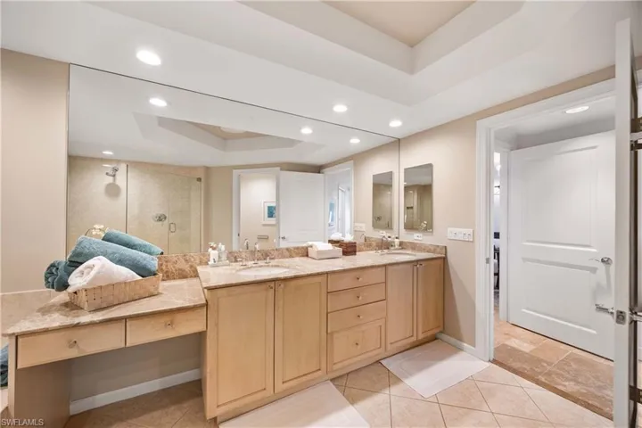 Bathroom with a shower stall, a raised ceiling, double vanity, recessed lighting, and light tile patterned floors