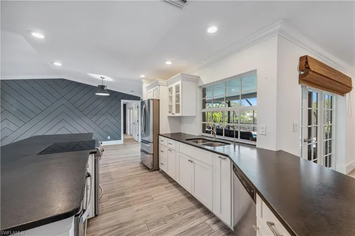 Kitchen with ornamental molding, a sink, light wood-style tile floors, appliances with stainless steel finishes, and dark countertops