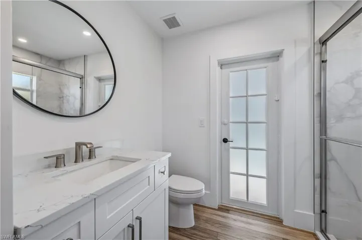 Bathroom with a marble finish shower, visible vents, toilet, wood tile finished floors, and vanity