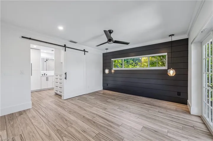 Unfurnished room featuring light wood-tile flooring, visible vents, ornamental molding, a ceiling fan, and a barn door