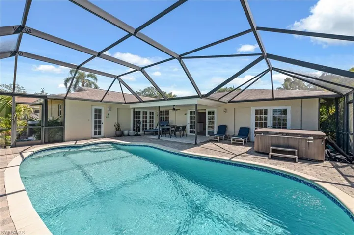 Outdoor pool with screen enclosure, a patio, a ceiling fan, and a hot tub