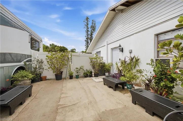 Concrete patio area featuring a white privacy fence and a white stucco building with a white side door and exterior lighting fixture