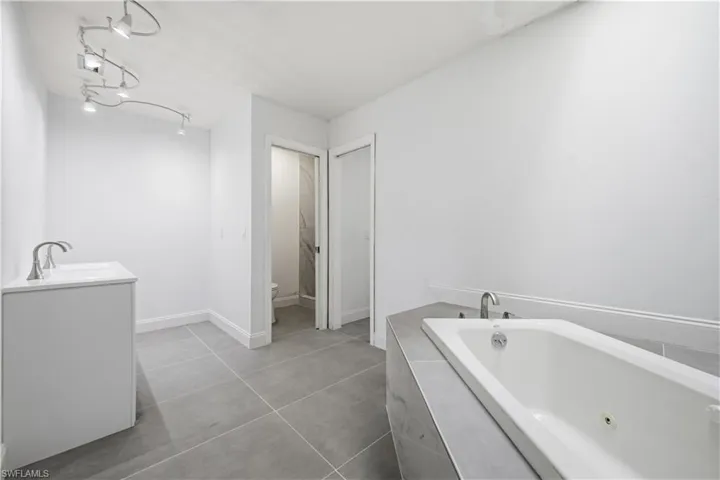Spacious bathroom featuring a built-in soaking tub, a vanity with a single basin, and track lighting