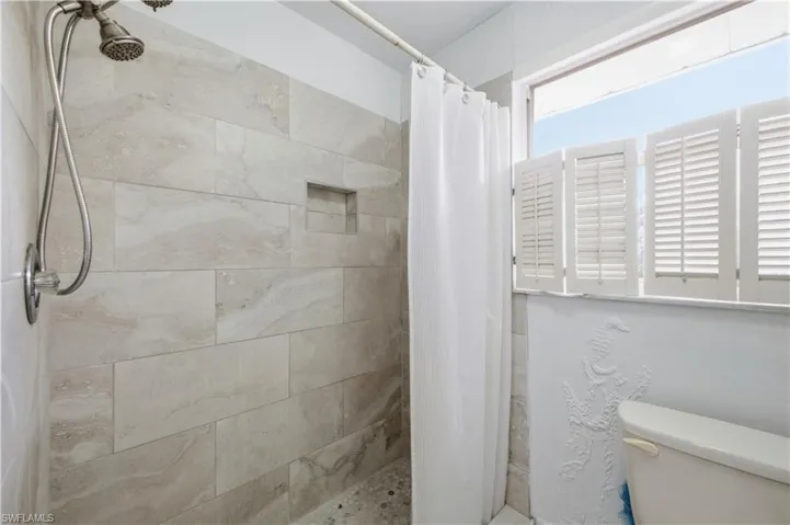 Shower featuring a handheld showerhead, textured wall tiling, and a recessed niche