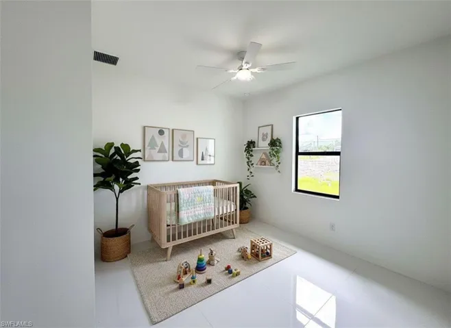 Bedroom featuring a nursery area, tile patterned flooring, and ceiling fan