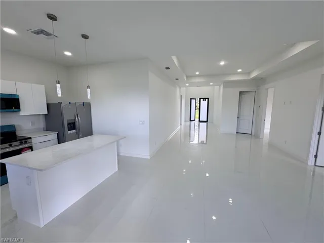 Kitchen featuring open floor plan, white cabinetry, appliances with stainless steel finishes, decorative light fixtures, and a kitchen island