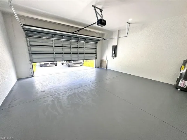 Garage featuring a textured wall, electric panel, and a garage door opener