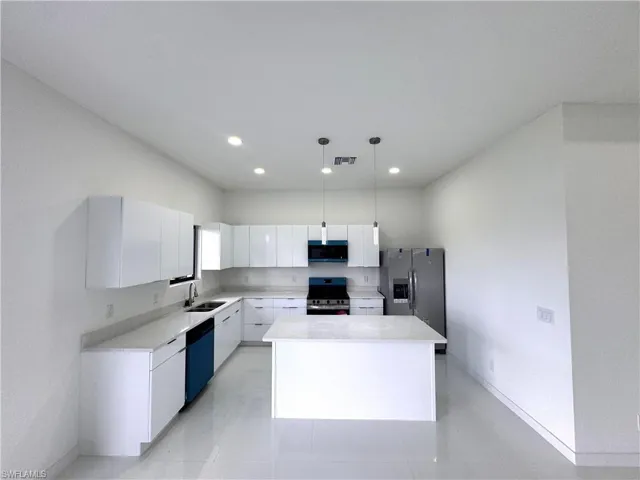 Kitchen with white cabinets, stainless steel fridge, modern cabinets, a kitchen island, and pendant lighting