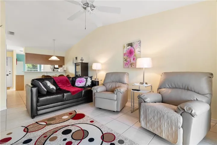 Living room featuring vaulted ceiling, ceiling fan, and light tile patterned flooring