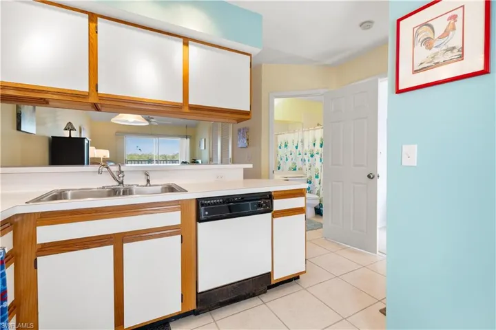 Kitchen with white cabinets, kitchen peninsula, dishwasher, light tile patterned floors, and sink
