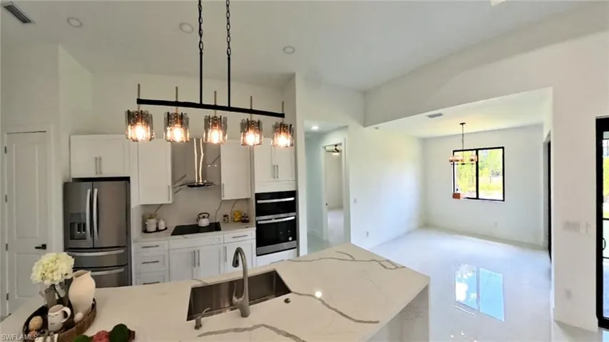 Kitchen featuring stainless steel refrigerator with ice dispenser, a sink, double oven, black electric stovetop, and exhaust hood