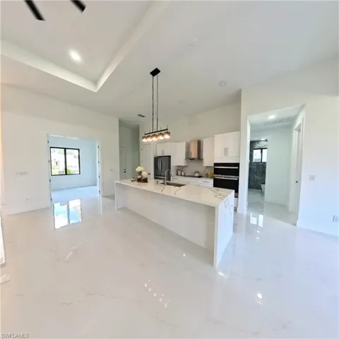 Kitchen featuring wall chimney exhaust hood, white cabinets, refrigerator with ice dispenser, a spacious island, and plenty of natural light