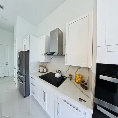 Kitchen featuring wall chimney exhaust hood, black appliances, light stone countertops, and white cabinetry