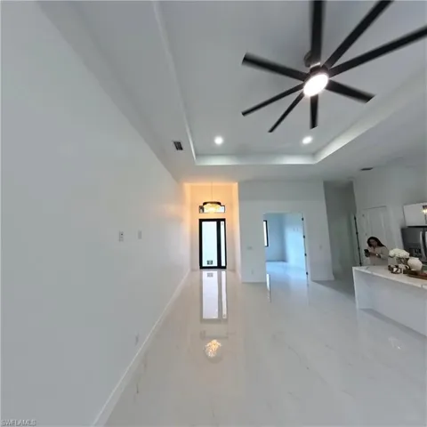 Unfurnished living room with a tray ceiling, a ceiling fan, recessed lighting, and baseboards