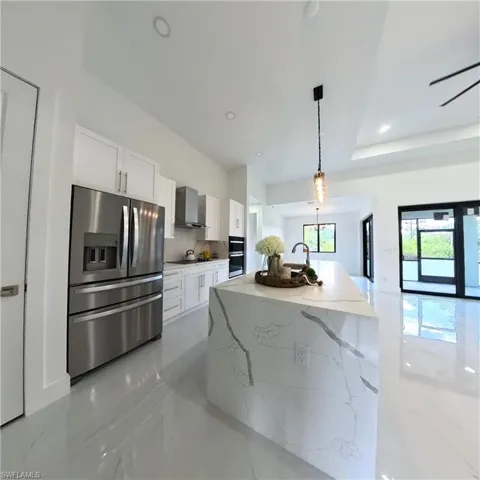 Kitchen with appliances with stainless steel finishes, wall chimney exhaust hood, white cabinets, light stone counters, and hanging light fixtures