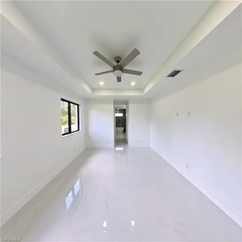 Empty room featuring a ceiling fan, recessed lighting, a tray ceiling, light marble finish flooring, and baseboards