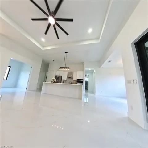 Unfurnished living room with a raised ceiling, a ceiling fan, and light marble finish floors