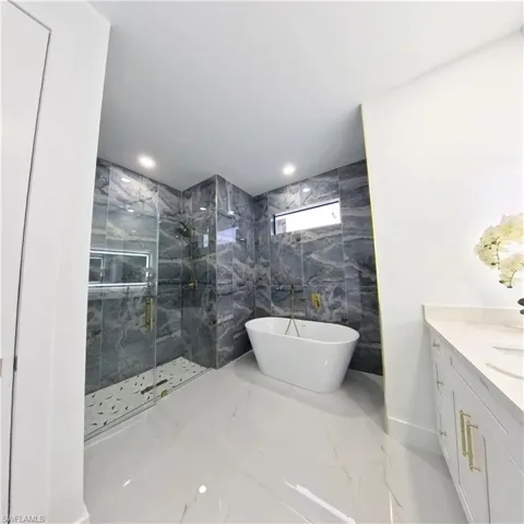 Bathroom featuring marble tiled flooring, a marble finish shower, a soaking tub, vanity, and recessed lighting