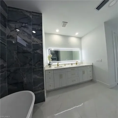Bathroom featuring marble look tiles, double vanity, a soaking tub, and recessed lighting