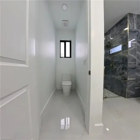 Bathroom with marble finish flooring, a marble finish shower, toilet, and baseboards