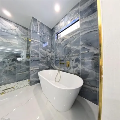 Full bathroom featuring tile walls, a soaking tub, marble tiled flooring, and a marble finish shower
