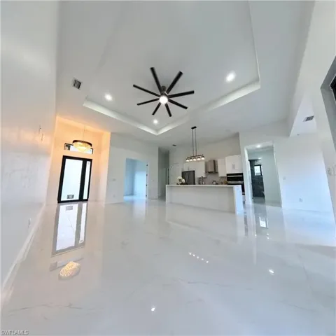 Unfurnished living room featuring a raised ceiling, ceiling fan, light marble finish flooring, and recessed lighting
