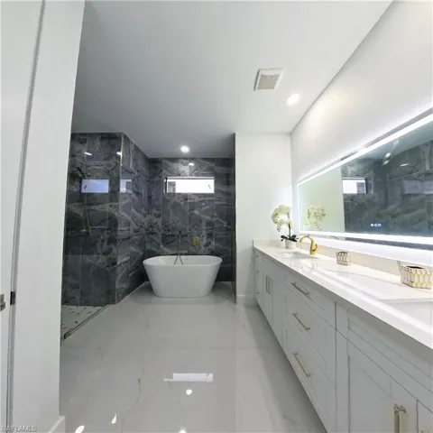 Full bathroom featuring marble tiled flooring, a marble finish shower, a soaking tub, double vanity, and recessed lighting