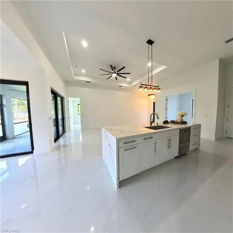 Kitchen featuring a tray ceiling, a sink, open floor plan, dishwasher, and a center island with sink