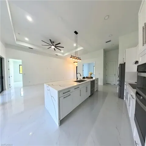 Kitchen featuring freestanding refrigerator, a sink, a raised ceiling, dishwashing machine, and open floor plan