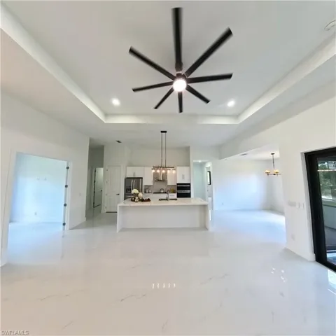Unfurnished living room with a chandelier, a raised ceiling, and ceiling fan