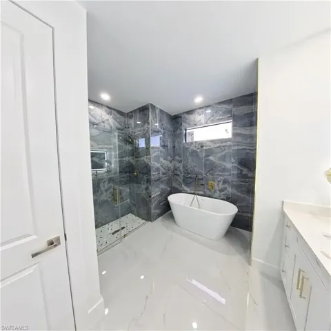 Full bathroom featuring marble tiled floors, a marble finish shower, a soaking tub, and vanity