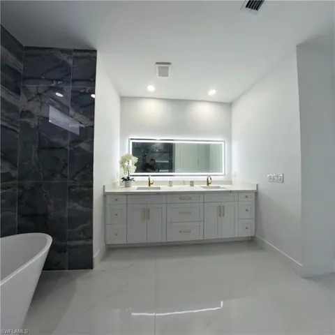 Full bathroom featuring marble tiled floors, double vanity, a freestanding bath, baseboards, and recessed lighting