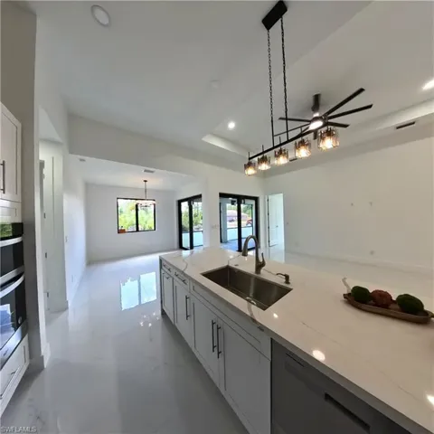 Kitchen featuring a sink, dishwashing machine, pendant lighting, light stone countertops, and recessed lighting