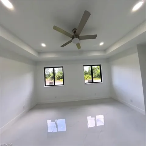 Unfurnished room with a raised ceiling, plenty of natural light, recessed lighting, ceiling fan, and baseboards