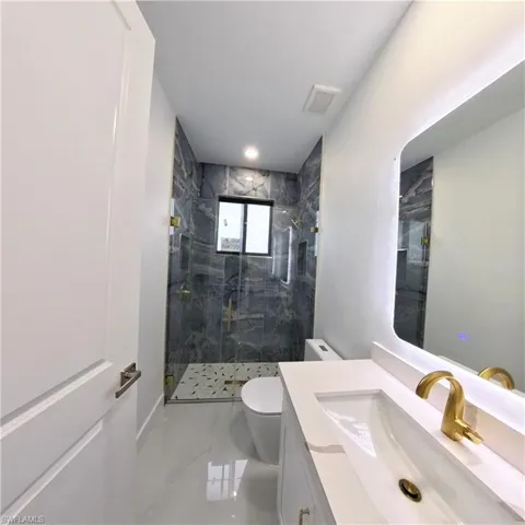 Bathroom featuring marble finish flooring, toilet, a marble finish shower, and vanity