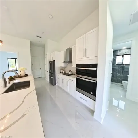 Kitchen featuring a sink, wall chimney range hood, black electric cooktop, and white cabinets