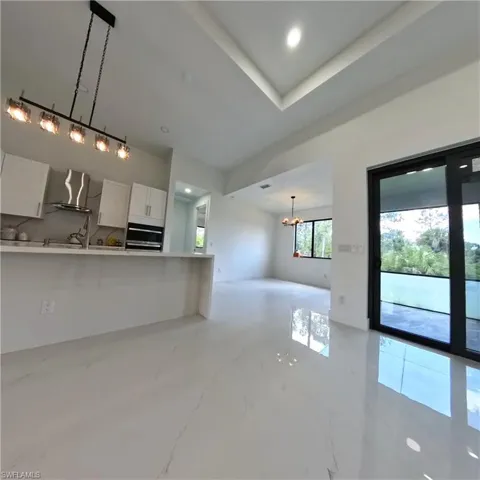 Kitchen with wall chimney range hood, wall oven, white cabinetry, modern cabinets, and a chandelier