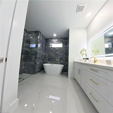 Bathroom with marble tiled floors, a marble finish shower, vanity, and a freestanding bath