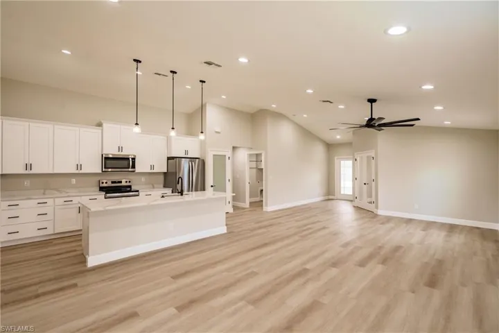 Kitchen with an island with sink, hanging light fixtures, vaulted ceiling, white cabinets, and appliances with stainless steel finishes