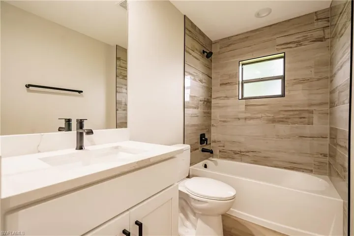 Full bathroom with vanity, tiled shower / bath combo, and toilet