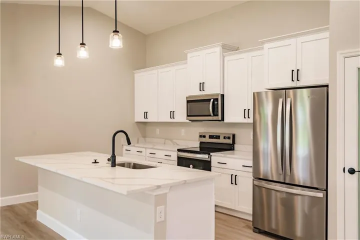 Kitchen with an island with sink, sink, light stone countertops, decorative light fixtures, and appliances with stainless steel finishes