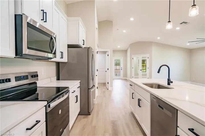 Kitchen featuring appliances with stainless steel finishes, sink, hanging light fixtures, and vaulted ceiling